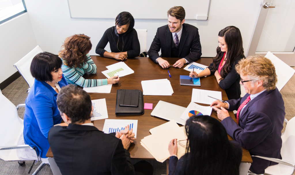 Mehrere Personen sitzen an einem runden Tisch mit Zetteln und Stiften und beraten